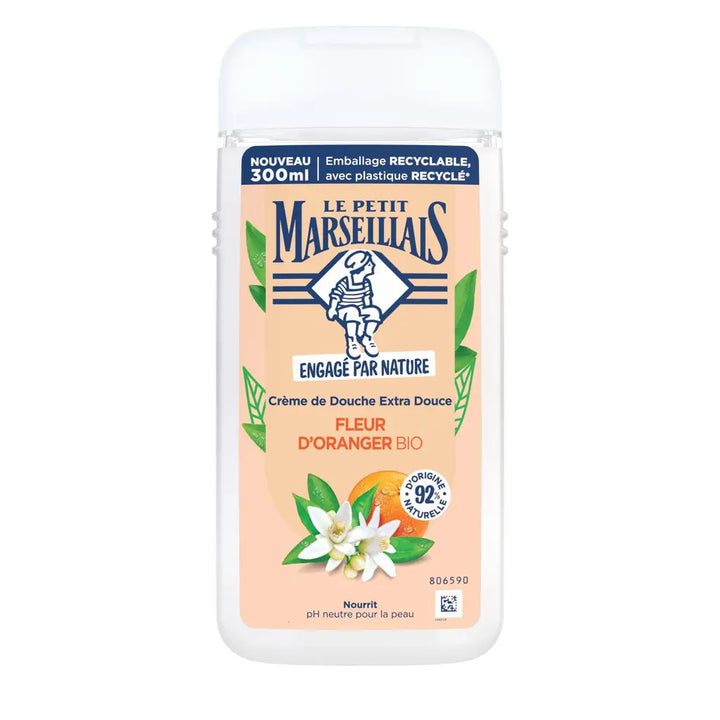 A 300ml bottle of Le Petit Marseillais Crème de Douche Extra Douceuse in 'Fleur d'Oranger' (Orange Blossom) scent. The product features a white plastic bottle with a peach-colored label, decorated with illustrations of orange blossoms, green leaves, and an orange slice.