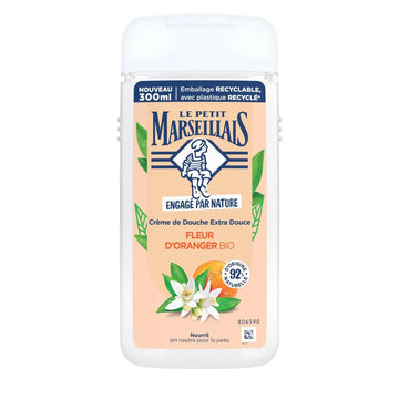 A 300ml bottle of Le Petit Marseillais Crème de Douche Extra Douceuse in 'Fleur d'Oranger' (Orange Blossom) scent. The product features a white plastic bottle with a peach-colored label, decorated with illustrations of orange blossoms, green leaves, and an orange slice.
